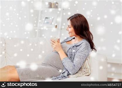 pregnancy, winter, rest, people and expectation concept - happy pregnant woman with cup drinking tea at home over snow