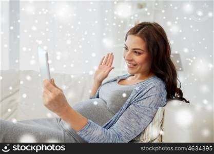 pregnancy, winter, technology, people and communication concept - happy pregnant woman with tablet pc computer having video call and waving hand at home over snow