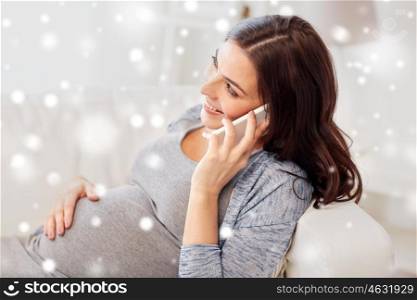 pregnancy, winter, technology, people and expectation concept - happy pregnant woman calling on smartphone at home over snow
