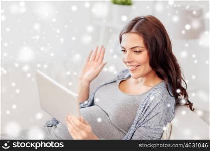 pregnancy, winter, technology, people and expectation concept - happy pregnant woman with tablet pc computer having video call and waving hand at home over snow