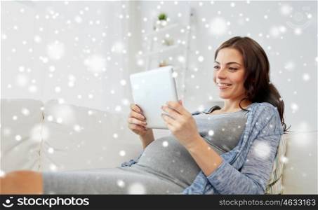 pregnancy, winter, technology, people and expectation concept - happy pregnant woman with tablet pc computer at home over snow