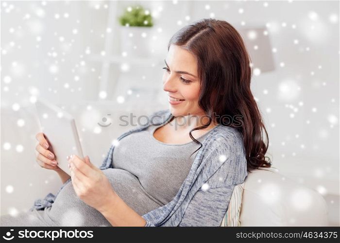 pregnancy, winter, technology, people and expectation concept - happy pregnant woman with tablet pc computer at home over snow
