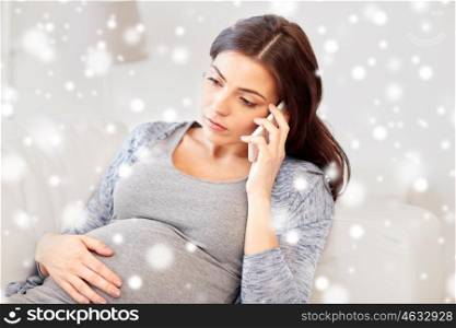 pregnancy, winter, technology, people and expectation concept - sad pregnant woman calling on smartphone at home over snow