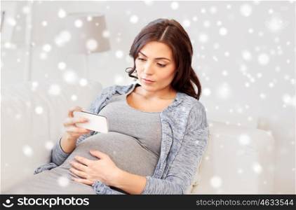 pregnancy, winter, technology, people and expectation concept - sad pregnant woman with smartphone at home over snow