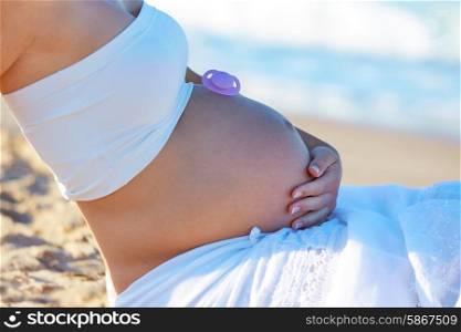 Pregnannt mother woman with pacifier on belly at the beach