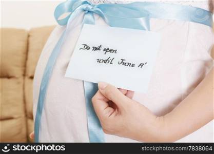 Pregnant belly with a light blue ribbon and a tag saying do not open until
