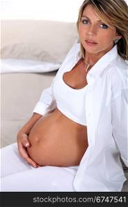Pregnant blond woman sat on bed