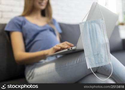 pregnant businesswoman couch working laptop with medical mask