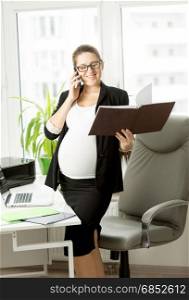 Pregnant businesswoman in black suit using mobile phone