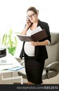 Pregnant businesswoman talking by phone and checking documents