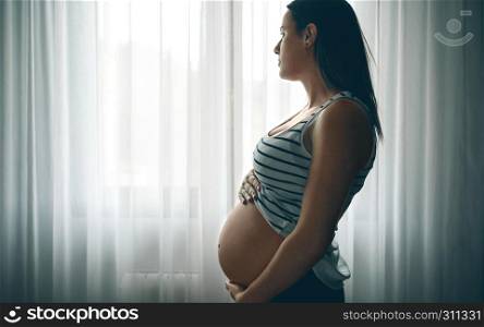 Pregnant caressing her nacked belly in front of a curtain. Pregnant caressing her nacked belly