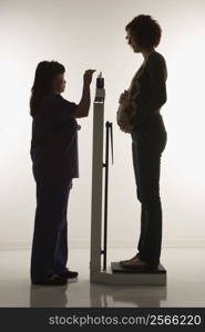 Pregnant Caucasian mid-adult woman being weighed by nurse.