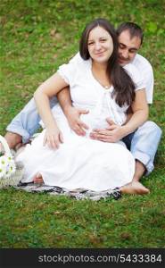 Pregnant couple are sitting on the grass in the park