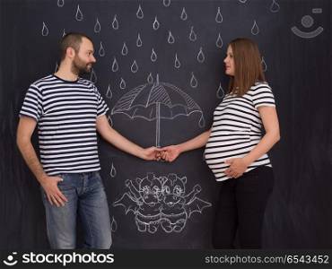 pregnant couple drawing their imaginations on chalk board. Conceptual photo of pregnant couple drawing their imaginations about the future life with children on chalk board
