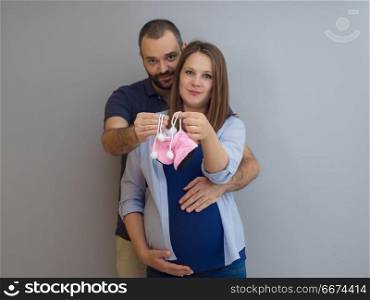 pregnant couple holding newborn baby shoes. young pregnant couple holding newborn baby shoes isolated on white background in family and parenthood concept