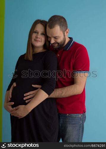 pregnant couple isolated over blue background. Portrait of a happy young couple,man holding his pregnant wife belly isolated over blue background