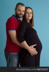 pregnant couple isolated over blue background. Portrait of a happy young couple,man holding his pregnant wife belly isolated over blue background