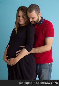 pregnant couple isolated over blue background. Portrait of a happy young couple,man holding his pregnant wife belly isolated over blue background