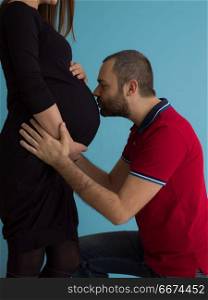 pregnant couple isolated over blue background. Portrait of a happy young couple,man holding his pregnant wife belly isolated over blue background
