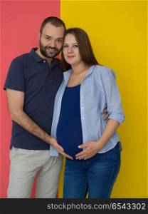 pregnant couple isolated over colorful background. Portrait of a happy young couple,man holding his pregnant wife belly isolated over colorful background