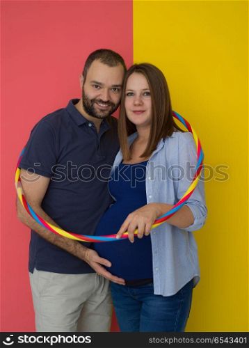 pregnant couple isolated over colorful background. Portrait of a happy young couple,man holding his pregnant wife belly isolated over colorful background