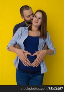 pregnant couple isolated over yellow background. Portrait of a happy young couple,man holding his pregnant wife belly isolated over yellow background