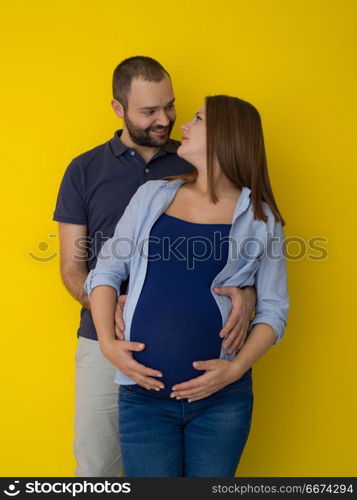 pregnant couple isolated over yellow background. Portrait of a happy young couple,man holding his pregnant wife belly isolated over yellow background