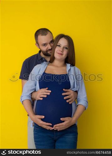 pregnant couple isolated over yellow background. Portrait of a happy young couple,man holding his pregnant wife belly isolated over yellow background