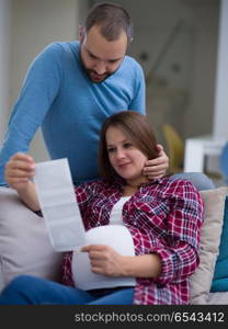 pregnant couple looking baby&rsquo;s ultrasound. Young pregnant couple looking baby&rsquo;s ultrasound photo while relaxing on sofa at home