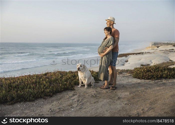 Pregnant couple on a wild beach and their dog expecting a baby