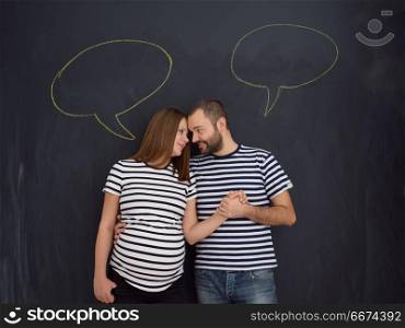 pregnant couple posing against black chalk drawing board. portrait of husband and pregnant wife posing against black chalk drawing board