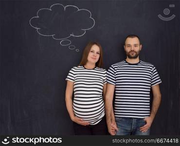 pregnant couple posing against black chalk drawing board. portrait of husband and pregnant wife posing against black chalk drawing board