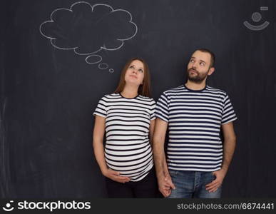 pregnant couple posing against black chalk drawing board. portrait of husband and pregnant wife posing against black chalk drawing board