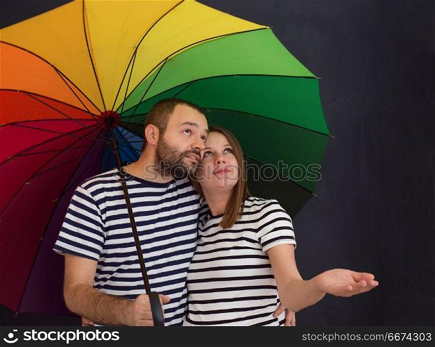 pregnant couple posing with colorful umbrella. portrait of husband and pregnant wife posing with colorful umbrella in front of black chalk drawing board