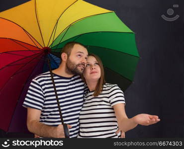 pregnant couple posing with colorful umbrella. portrait of husband and pregnant wife posing with colorful umbrella in front of black chalk drawing board