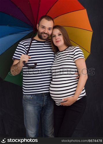 pregnant couple posing with colorful umbrella. portrait of husband and pregnant wife posing with colorful umbrella in front of black chalk drawing board