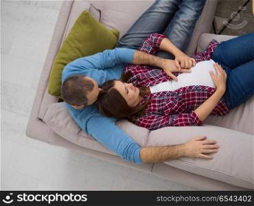 pregnant couple relaxing on sofa. top view of happy pregnant couple relaxing on sofa couch at home