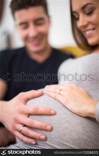 Pregnant Couple Sitting On Sofa With Man Touching Womans Stomach