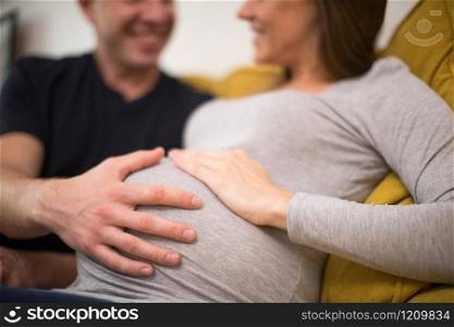 Pregnant Couple Sitting On Sofa With Man Touching Womans Stomach