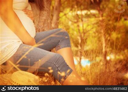 Pregnant female relaxing in autumnal park, sitting down near tree, enjoying autumn nature, body part, sunny day, happy and healthy pregnancy concept