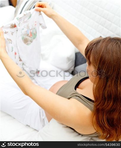 pregnant female relaxing on sofa at home and holding baby clothes in hands. Closeup.&#xA;