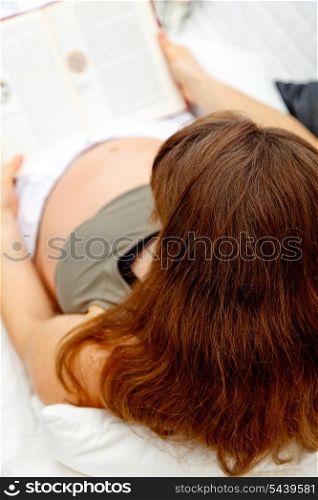 Pregnant female relaxing on sofa at home with book. Close-up.&#xA;