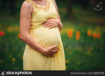 Pregnant girl in a yellow dress hugging her stomach in the field.. Pregnant girl in a yellow dress hugging her stomach in the field