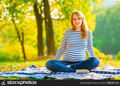Pregnant girl in jeans and a striped sweater resting in a park