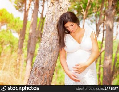 Pregnant girl in summer forest looking on her abdomen and touching it, new young family, walking in the park, happy pregnancy concept