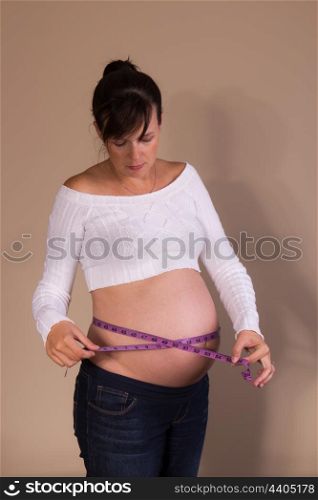 Pregnant girl measuring her belly with a measuring tape