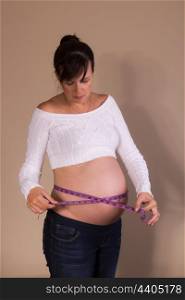 Pregnant girl measuring her belly with a measuring tape
