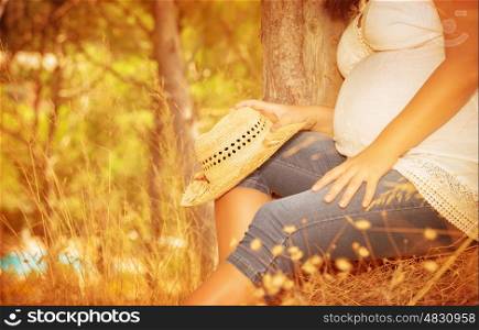 Pregnant girl sitting in autumnal park, body part, tummy of expectant woman, spending time in countryside, healthy pregnancy concept