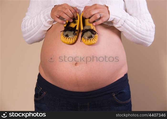 Pregnant girl with baby shoes on her exposed belly