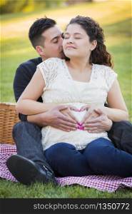 Pregnant Hispanic Couple Making Heart Shape with Hands on Belly in The Park Outdoors.